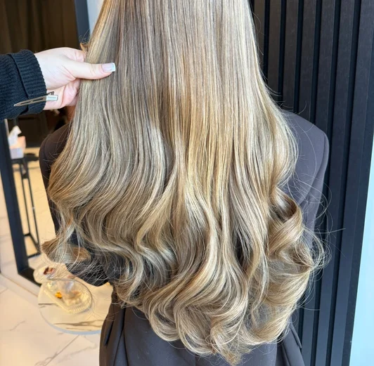 Blonde balayage extensions met zachte krullen en dimensionale highlights